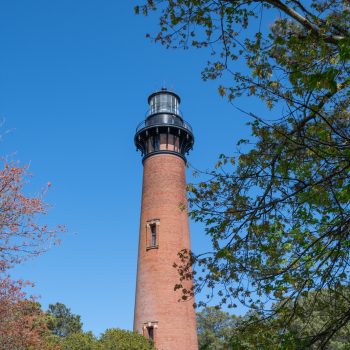 Currituck Beach Lighthouse in Corolla, North Carolina, showcasing its tall red brick structure against a clear blue sky