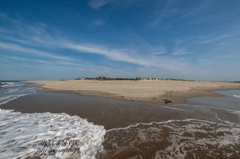 A sandy beach stretches along the coastline under a clear blue sky, with gentle waves lapping at the shore